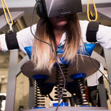 A rig for simulating scuba diving. A person is lying down on a spring table and is wearing an Oculus Rift headset with arms suspended from the rig through elastic bands.